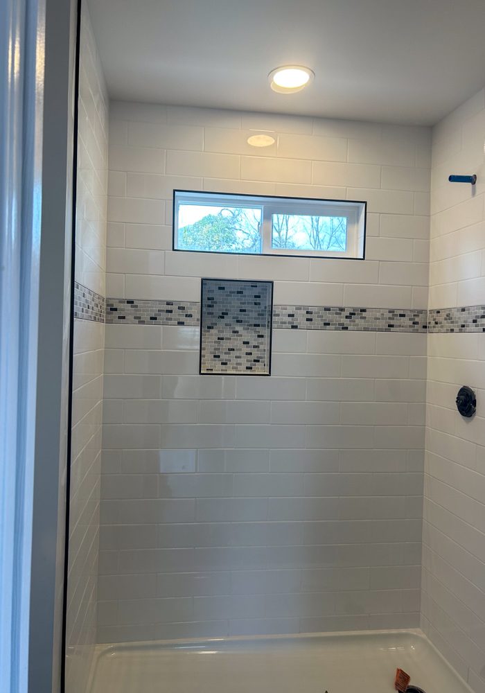 A bathroom remodeled, with upgraded tile backsplash, a shower niche, and fixtures yet to be installed.