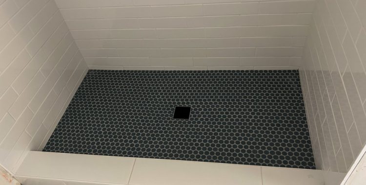 An offset tile pattern installed as shower backsplash and mini hexagonal patterned tiles for the flooring