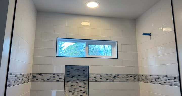 A bathroom remodeled, with upgraded tile backsplash, a shower niche, and fixtures yet to be installed.