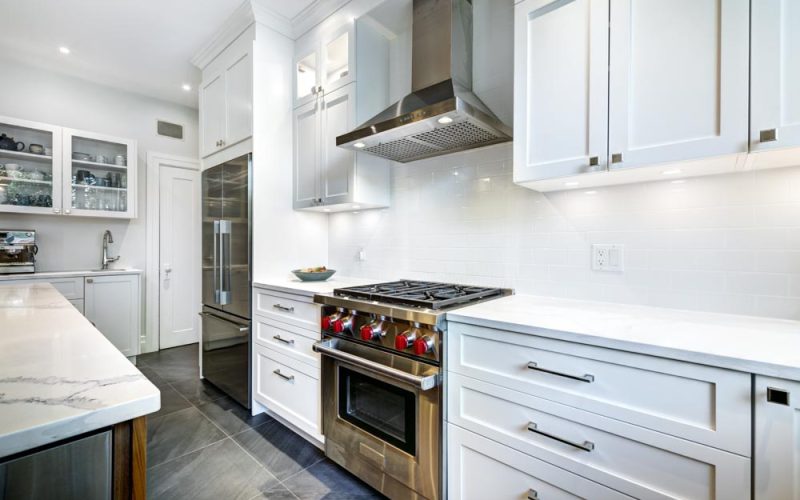 A newly renovated kitchen with white cabinets, gray tile flooring, and marble countertops