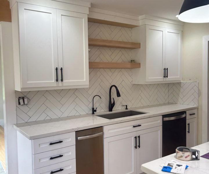 Chevron tile backsplash installed in the kitchen with wall mounted wood shelves in between cabinets