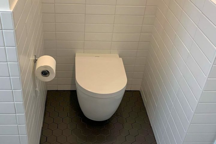The toilet area of a bathroom with tile flooring and backsplash