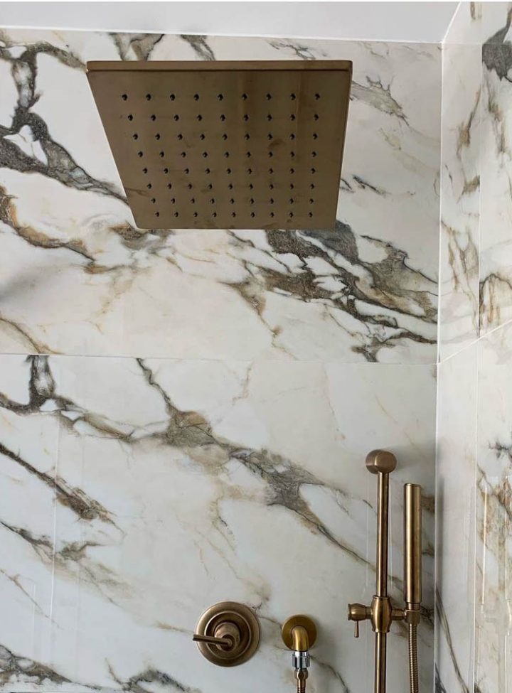 Tile installed as shower backsplash and brass shower fixtures